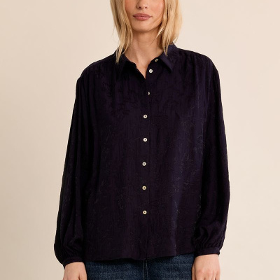 Blusa preta texturizada de manga longa com botões brancos e calças de ganga azuis.