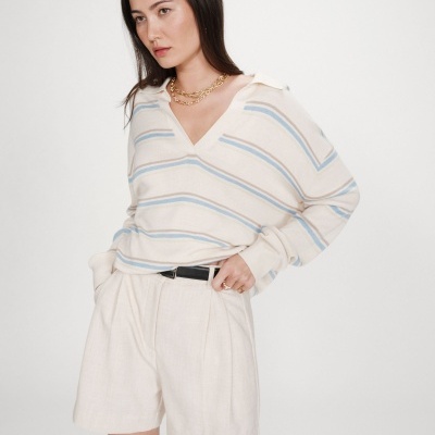 Mulher com blusa creme às riscas azuis e castanhas e calções creme com cinto preto.