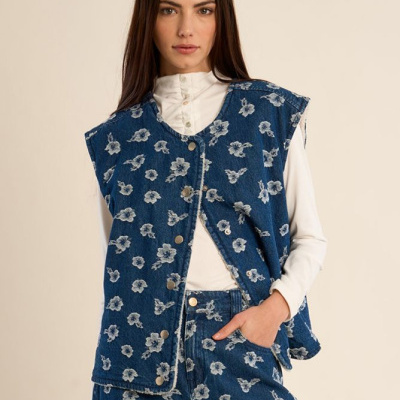 Conjunto azul de ganga com padrão floral branco, colete e calças, e camisa branca de manga comprida por baixo.