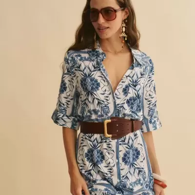 Mulher com vestido branco e azul, cinto castanho, óculos de sol e brincos grandes