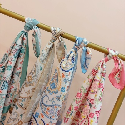 Cinco lenços coloridos com padrões florais pendurados em barra dourada
