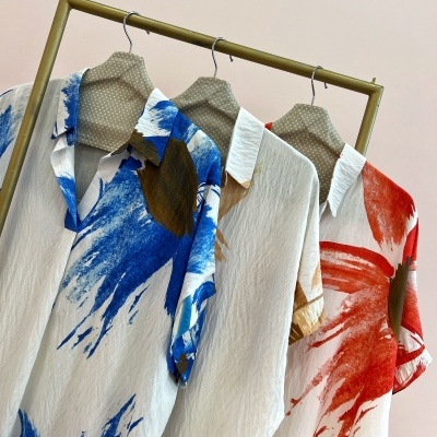 Três camisas coloridas penduradas em cabides num varão cor bege