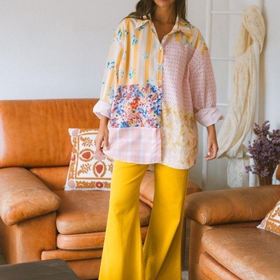 Camisa patchwork colorida e calças amarelas largas em sala com sofá de couro castanho.