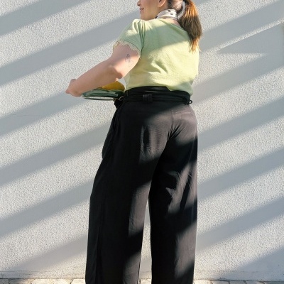 Mulher de costas com t-shirt verde, calças pretas largas e sapatilhas brancas a segurar prato verde com fundo branco e sombras diagonais.