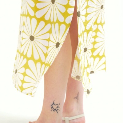 Vestido amarelo com flores brancas e sandálias brancas nas pernas.
