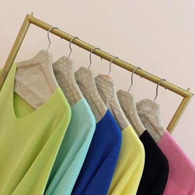 Seis camisolas de malha coloridas penduradas em cabides de tecido bege em varão de madeira