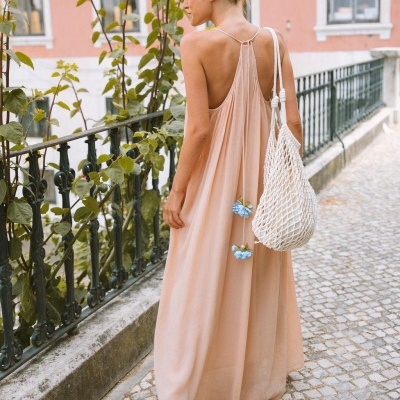 Mulher de costas com vestido longo pêssego e bolsa de rede branca numa calçada urbana
