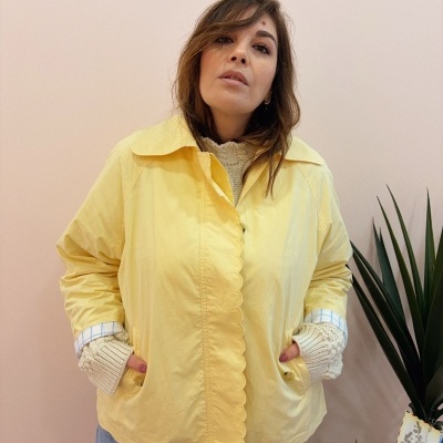 Mulher com casaco amarelo e calças jeans junto a planta verde