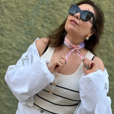 Mulher com óculos de sol, lenço ao pescoço, top branco com riscas pretas, casaco e calça brancos