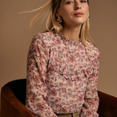 Blusa rosa floral com folhos usada por mulher sentada numa cadeira castanha