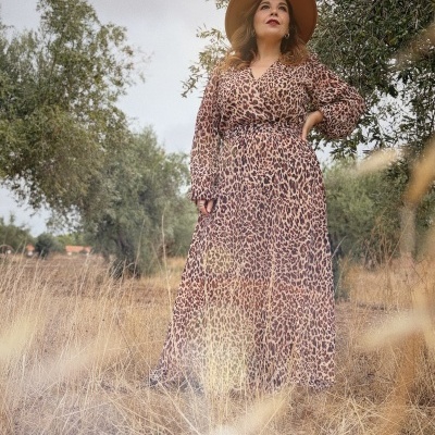 Mulher com vestido comprido animal print e chapéu castanho em ambiente natural