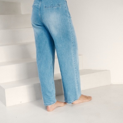 Calças de ganga azul claro com bolso falso na parte traseira e cintura alta da pessoa de pé descalça junto a escadas brancas