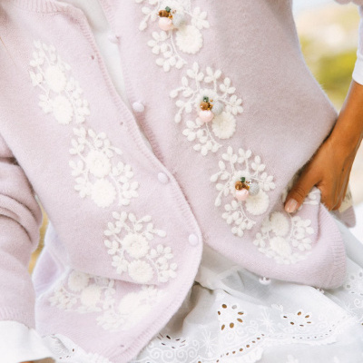 Camisola rosa clara com bordados florais brancos e aplicações decorativas, usada com vestido branco bordado.
