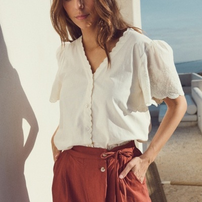 Blusa branca feminina com botões e calças cor terracota com laço na cintura num cenário exterior
