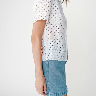 Blusa branca de manga curta com padrão bordado e saia azul clara de ganga.