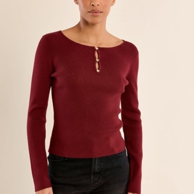Camisola vermelha de malha fina com botões decorativos e calças pretas.