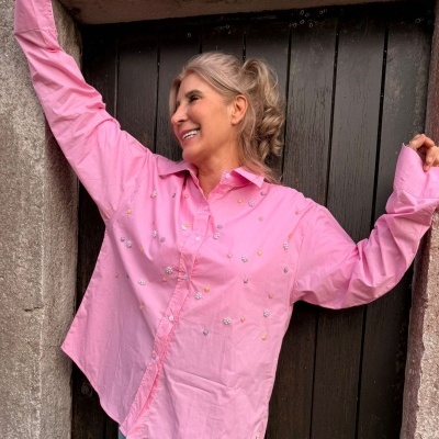 Mulher com camisa rosa decorada em frente a porta de madeira escura