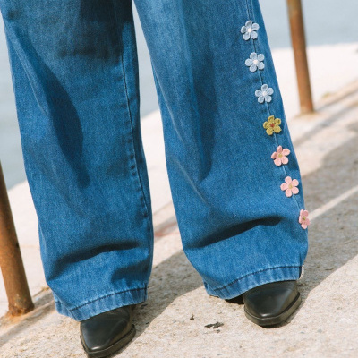 Calças de ganga azuis largas com flores bordadas coloridas na lateral e sapatos pretos