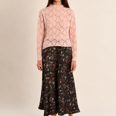 Mulher com blusa de renda rosa e saia preta floral, sandálias pretas de salto alto