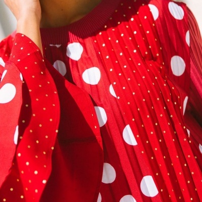 Blusa vermelha com bolinhas brancas e douradas, pregas e gola canelada.