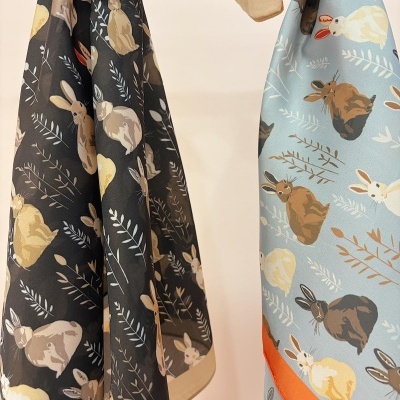 Tecidos com padrão de coelhos, uma peça preta e outra azul claro com borda laranja.