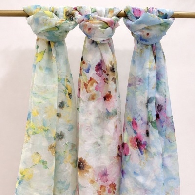 Três lenços florais em tecidos leves pendurados num cabide de madeira.