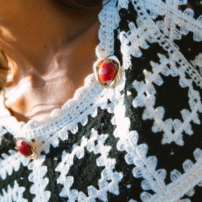 Detalhe de vestido preto com croché branco e botões vermelhos e dourados no decote
