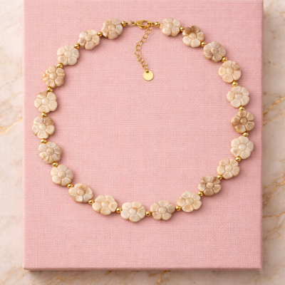 Colar de flores bege e contas douradas sobre fundo rosa e mármore