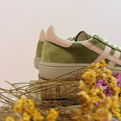 Ténis baixos em camurça verde e rosa sobre livros com flores secas amarelas.