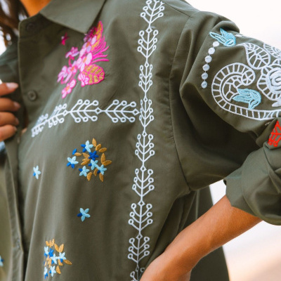 Camisa verde militar com bordados florais coloridos e padrões geométricos bordados.