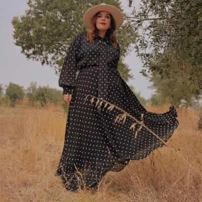 Vestido comprido preto com bolinhas brancas usado por mulher com chapéu bege ao ar livre