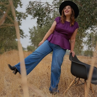 Mulher com blusa roxa, calças de ganga e chapéu preto em ambiente natural