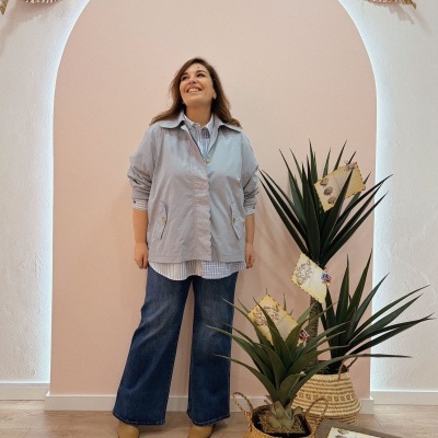 Mulher com casaco azul claro e jeans largos junto a plantas em vasos