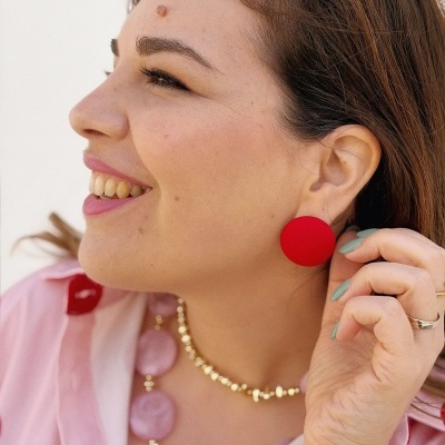 Mulher com brinco redondo vermelho e colar rosa usando camisa rosa com padrão vermelho