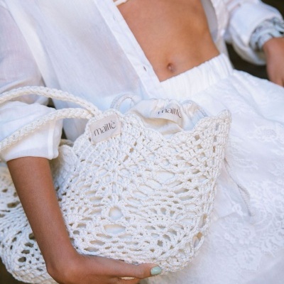 Sacola branca de crochê com etiquetas maittè segurada por mulher de roupa branca.