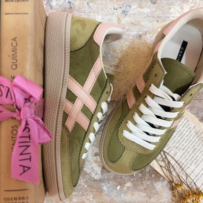 Sapatilhas verdes e cor de rosa em camurça com atacadores brancos sobre chão de pedra