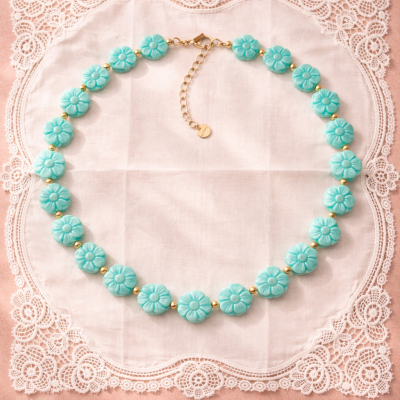 Colar de flores azuis e contas douradas sobre pano bordado rendado