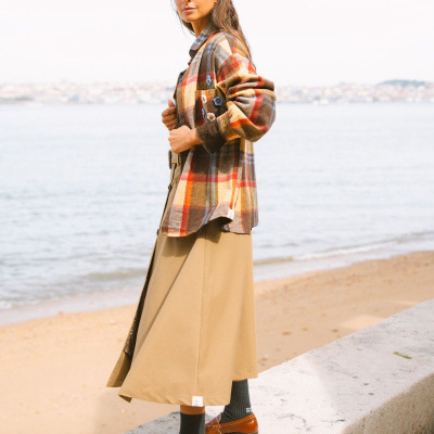 Camisa xadrez castanha com bordados florais, saia bege, meias pretas e sapatos marrons na praia
