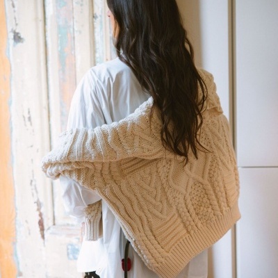 Mulher com suéter bege de malha grosso sobre os ombros e camisa branca vista de costas