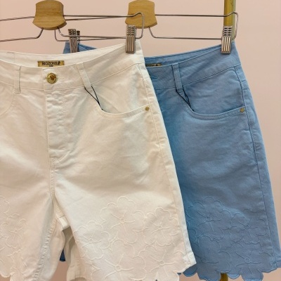 Dois calções de ganga branco e azul claro com padrão floral bordado pendurados em cabides de madeira num varão amarelo