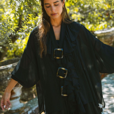 Mulher a usar top preto fluído com folhos e fivelas grandes em ambiente exterior verde