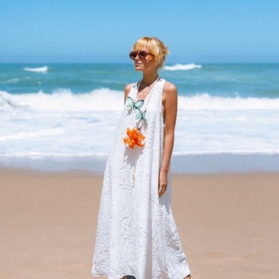 mulher com vestido longo branco e colar de flores na praia