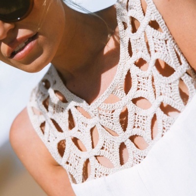 Vestido branco com detalhe em croché na parte superior usada por mulher com óculos escuros.