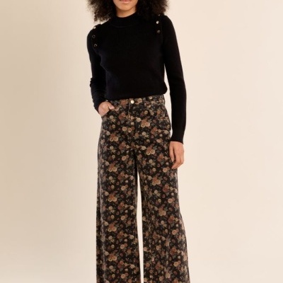 Mulher com camisola preta de malha e calças largas florais e sapatos pretos.