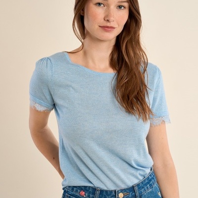 Mulher com t-shirt azul clara de manga curta com renda nas mangas e jeans azul bordado.