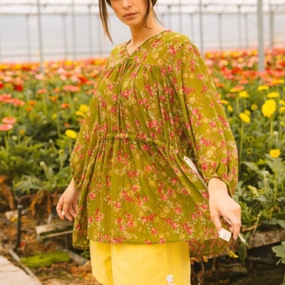 Blusa verde com flores rosa e calções amarelos em estufa de flores