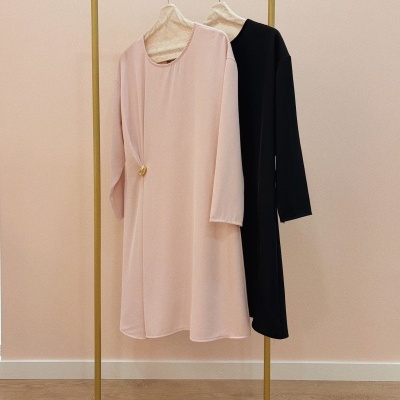 Duas túnicas em rosa claro e preto penduradas em cabides forrados, suporte metálico dourado, fundo rosa