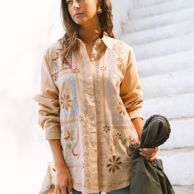 Camisa bege bordada com padrões florais coloridos e mulher segurando casaco verde