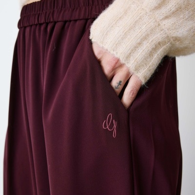 Calças vinho com cós elástico e bordado rosa claro com camisola bege de malha.
