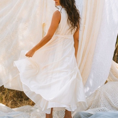 Vestido comprido branco fluido com sandálias castanhas em cenário com tecidos brancos
